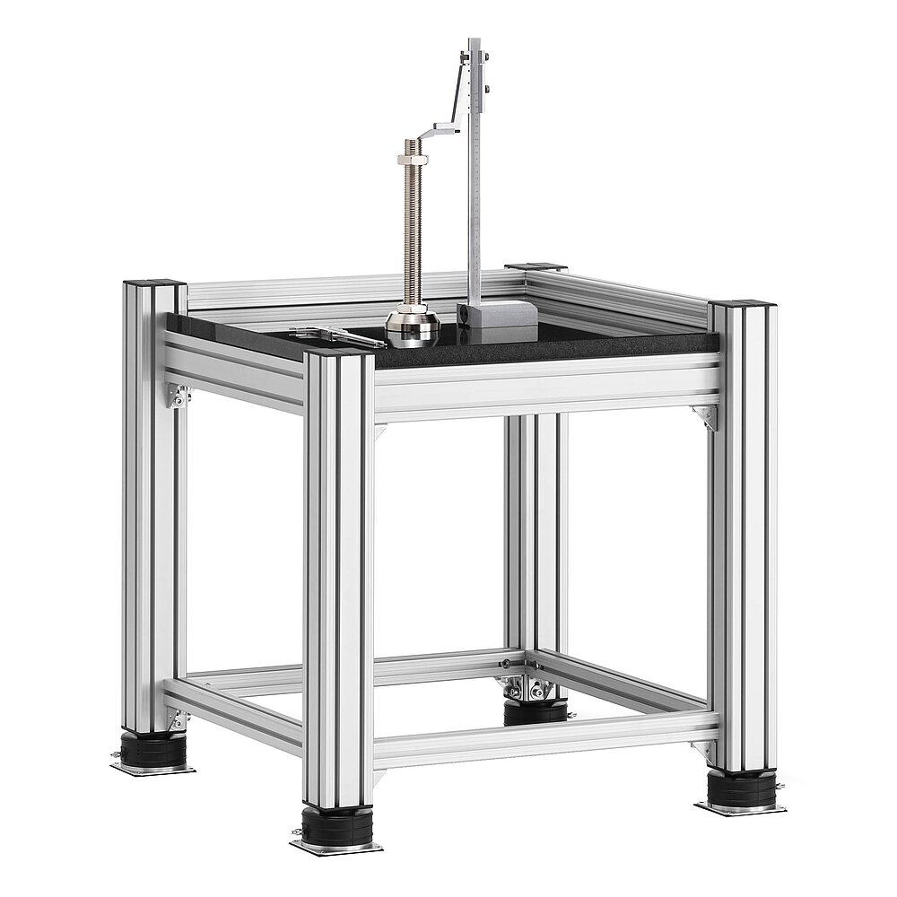a square, cube-shaped metrology table made of aluminium profiles, with thick black granite table top, mounted on black air-cushion vibro-mounts FLN, and with precision height marker, calliper and levelling element placed on the granite table top, isolated on white background