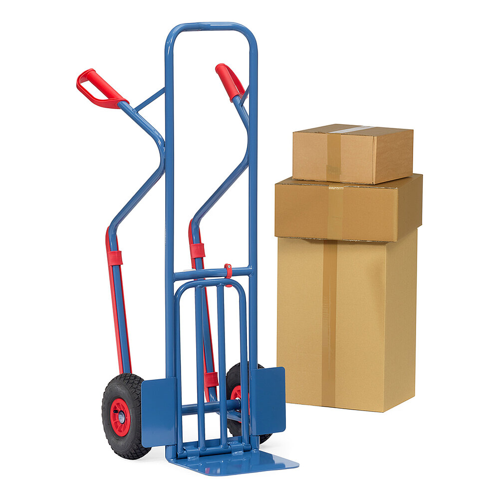 a blue FETRA® parcel cart with air tyres, folded up steel tube loading fork, bent support skids for horizontal positioning and red handles, next to a stack of cardboard boxes, isolated on white background