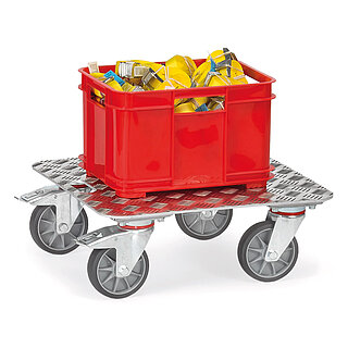 a FETRA® dolly with low, rectangular platform made of sturdy aluminium sheet metal with cross-wise Quintett-structure, rounded corners and recessed grip, below four steering wheels, the rear ones fastenable, and loaded with a red plastic box with yellow lashing straps, isolated on white background