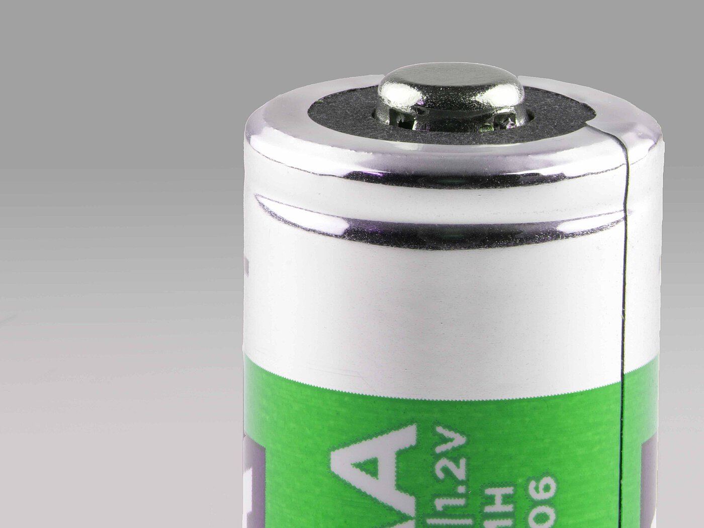 the silvery shining anode and the upper, greenish-metallic half of a rechargeable battery of standard size AAA as a close-up fotography on a grey background