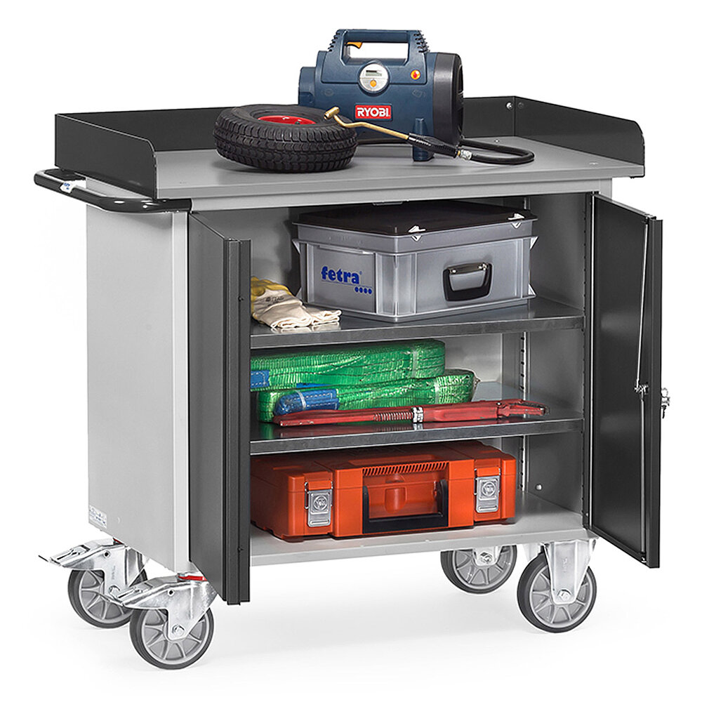 a grey FETRA® workshop cart with skirting, displaying two opened cupboard doors, roll-off protection skirting on three sides, and loaded with various utensils, isolated on white background