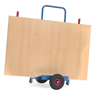 a blue FETRA® cart for the transport of sheet material, with two black rubber tyres, two red handles and loaded with a large brown wooden board, isolated on white background