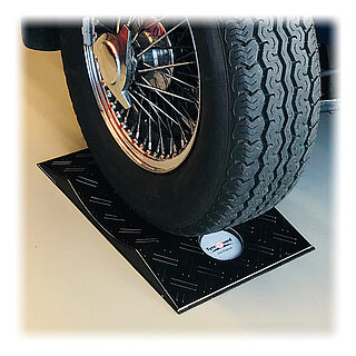a black concave-shaped TyreGuard® tyre protector made of high-strength plastics and with anti-slip mat, underneath a tyre mounted on a classic-style chromed spoke hub