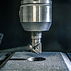 detail view of a vertical drill chuck inside a CNC milling machine, equipped with a thread milling head which has milled a thread into a grey cast iron part placed underneath