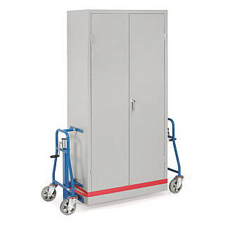 two blue FETRA® furniture lifting rollers made of steel tubes with two transport wheels each, crank shaft at the rear, and felt-lined carry-loops at the bottom and supports on top, in between levitating a grey sheet metal cupboard, fastened to the rollers securely with a red lashing strap, isolated on white background