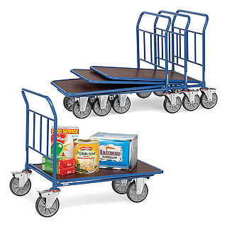 a composition of four blue FETRA® platform trolleys, each with push bar made from steel tube, two fixed wheels at the front, two fastenable steering wheels at the rear and brown wooden loading platform, three carts stacked into each other and the front single one loaded with various food articles, isolated on white background