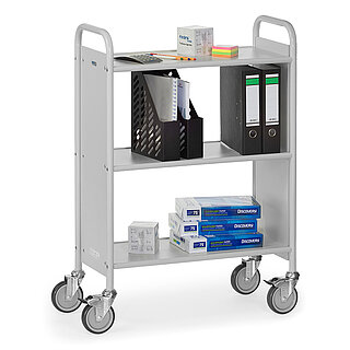 a light-grey FETRA® office trolley made of steel tube, with three storeys of grey wooden shelvings, grey side walls and four steering wheels, two of which can be fastened, and the shelvings filled with various office materials and files, isolated on white background